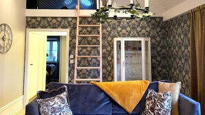 Ein Wohnzimmer mit einem blauen Sofa, gemusterten Kissen, einer gelben Decke, einer Holzleiter und einem Kronleuchter.