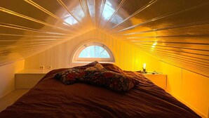 Ein kleines Schlafzimmer im Dachgeschoss mit niedrigem Giebeldach, einem Bett, einem Nachttisch und einem Fenster.
