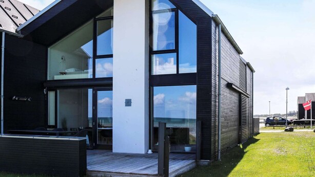 A modern building with large glass windows, a flat roof, and a wooden deck. - 8 Person Holiday Home in Hadsund (Hadsund)