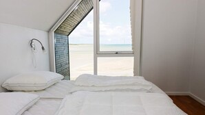 A bedroom with a large window overlooking a beach, a bed with white bedding, and a wall-mounted device. - 8 Person Holiday Home in Hadsund (Hadsund)