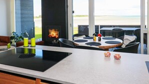 A modern kitchen with a central island, a built-in fireplace, and a dining area with a view of the beach. - 8 Person Holiday Home in Hadsund (Hadsund)