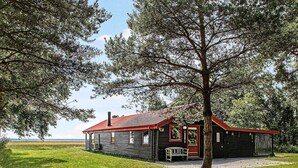 A rustic cabin with a red roof, surrounded by lush greenery and a clear sky. - 4 Person Holiday Home in Laeso (Læsø)