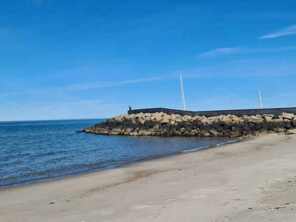 A coastal scene with a rocky breakwater and a clear blue sky.