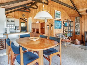 A wooden interior with a round dining table, blue chairs, a kitchen area, and a fireplace.