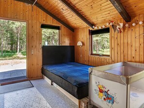 A wooden cabin interior with a single bed, a small table, and two windows.