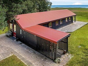 A two-story log cabin with a red metal roof, a porch with a bench, and a view of the ocean. - 4 Person Holiday Home in Laeso (Læsø)