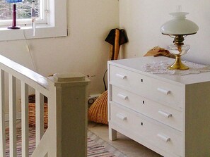 A room with a white dresser, a lamp on top, a window with blinds, a wicker basket, and a wooden chair. - 4 Person Holiday Home in Ed (Ed)