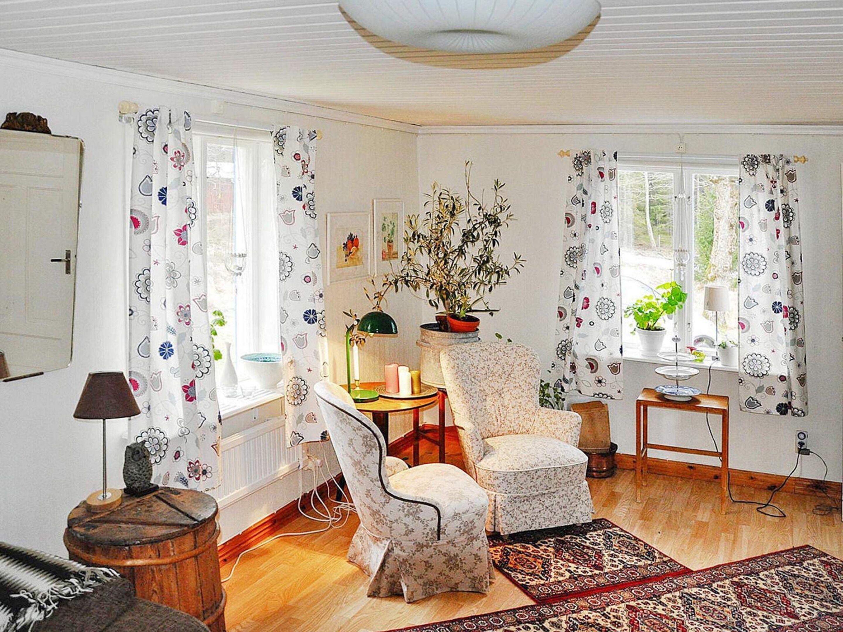 A room with a floral-patterned chair, a table with a lamp, a potted plant, and a rug.