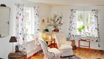 A room with a floral-patterned chair, a table with a lamp, a potted plant, and a rug.
