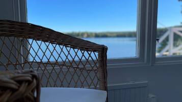 A wicker chair with a white cushion in front of a window overlooking a body of water.