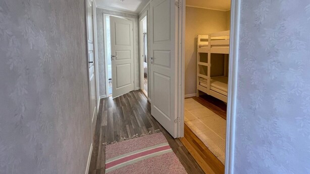 Un pasillo con piso de madera, puertas blancas y una cama litera en la habitación contigua.