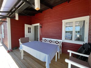 A covered outdoor area with a table and chairs, a door, and a window overlooking a body of water. - 4 Star Holiday Home in Bruzaholm (Bruzaholm)