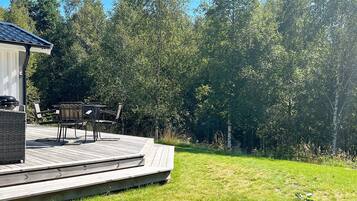 A deck with outdoor furniture, a barbecue grill, and a view of a forested area.