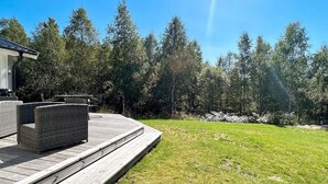 A deck with outdoor furniture, a grassy lawn, and a forested area in the background. - 4 Person Holiday Home in Hacksvik (Håcksvik)