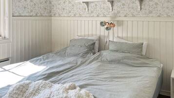 A single bed with a striped bedspread and pillows, a white headboard, and a green vase on a shelf above.