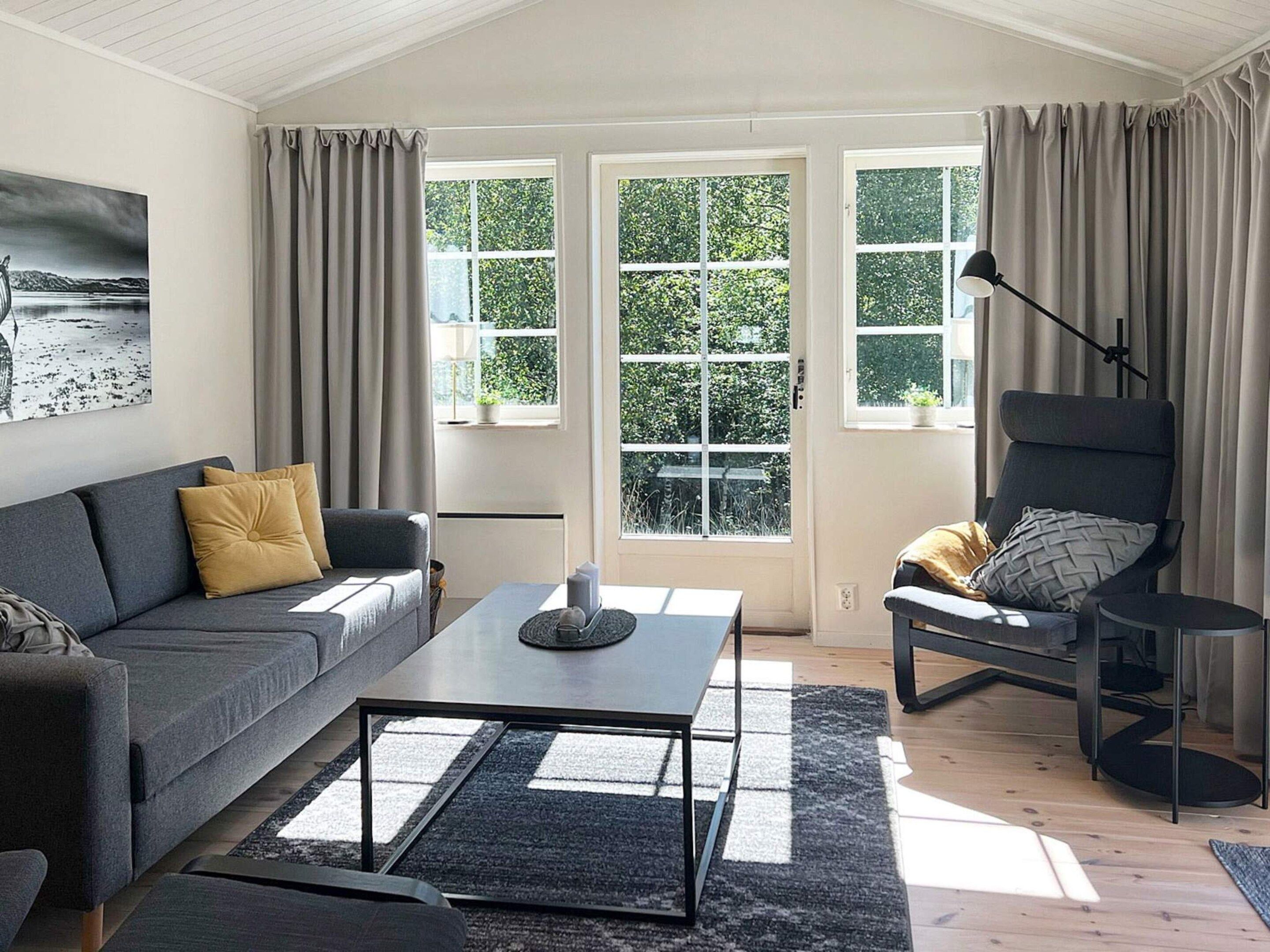 A modern living room with a sofa, armchair, coffee table, and a view through large windows.