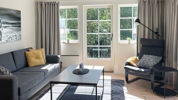 A modern living room with a sofa, armchair, coffee table, and a view through large windows.