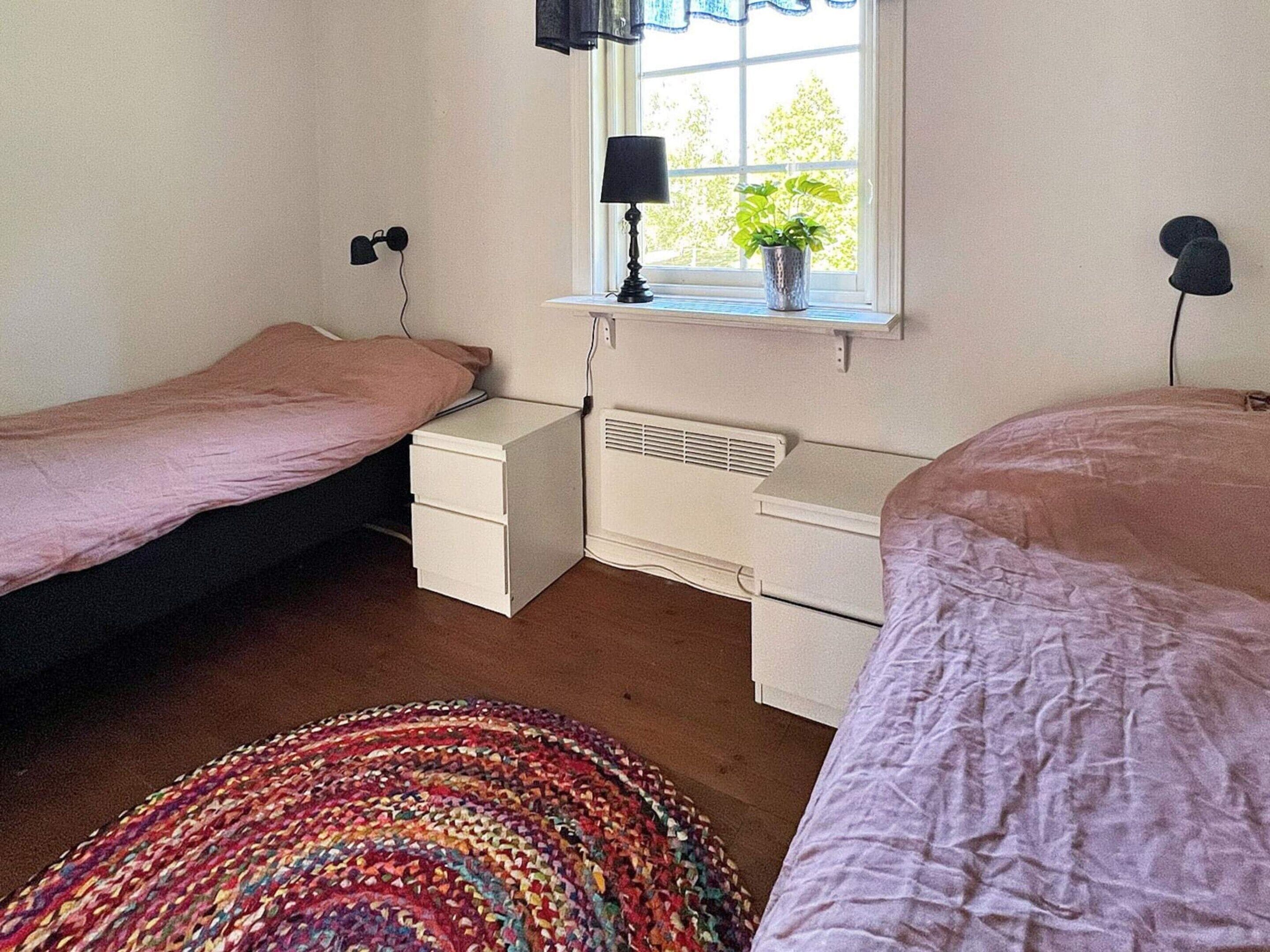 A bedroom with two single beds, a bedside table with a lamp, a window with a view, and a radiator.