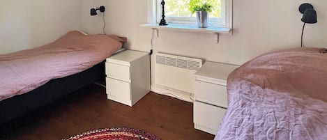 A bedroom with two single beds, a bedside table with a lamp, a window with a view, and a radiator.