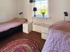 A bedroom with two single beds, a bedside table with a lamp, a window with a view, and a radiator. - 4 Person Holiday Home in Hacksvik (Håcksvik)