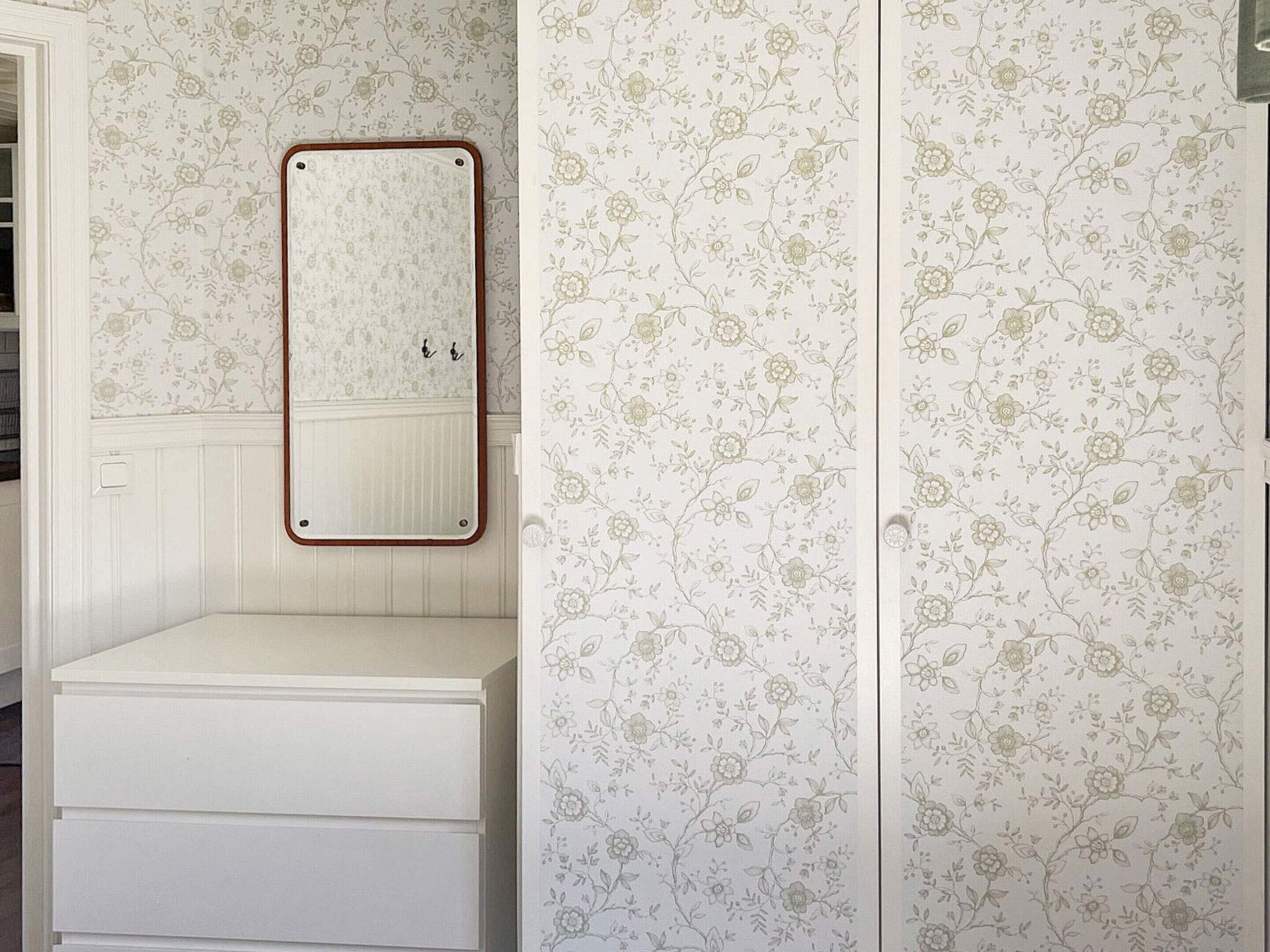 A bathroom with a white vanity, a mirror with a wooden frame, and floral wallpaper.