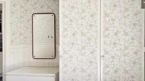 A bathroom with a white vanity, a mirror with a wooden frame, and floral wallpaper. - 4 Person Holiday Home in Hacksvik (Håcksvik)