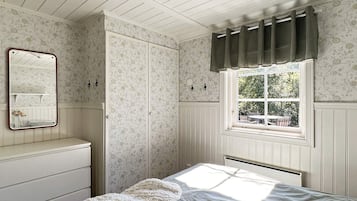A bedroom with a bed, a dresser, a mirror, a window with curtains, and a radiator.