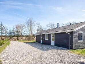A single-story building with a gravel driveway leading to a wooden door.