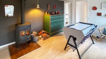 Quarto com lareira a lenha, uma cômoda verde e uma mesa de futebol.