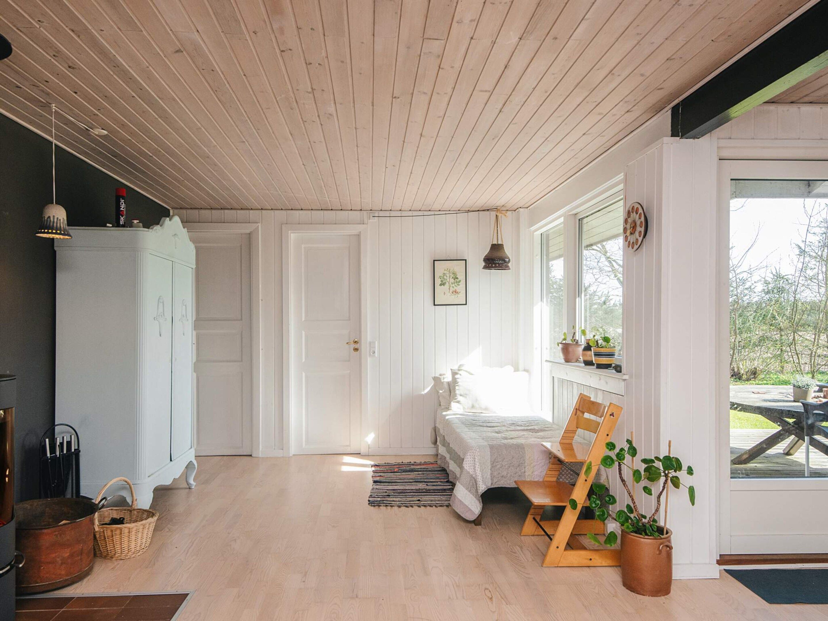 Une pièce comprenant un lit, une chaise en bois, une armoire et une fenêtre donnant sur l’extérieur.