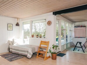 Une pièce comprenant un lit, une chaise en bois, une plante en pot, une fenêtre et une porte donnant sur un espace extérieur.