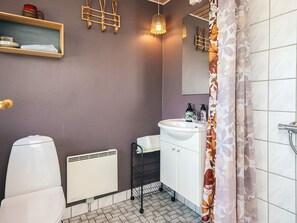 A bathroom with a toilet, a sink, a mirror, a shower curtain, a radiator, and a shelf with a red mug.