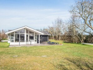 Une maison moderne dotée d’une grande extension en verre, d’un patio avec mobilier d’extérieur et d’une pelouse verdoyante tout autour.