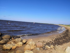 Una playa con rocas grandes al frente, una orilla arenosa y el océano al fondo.
