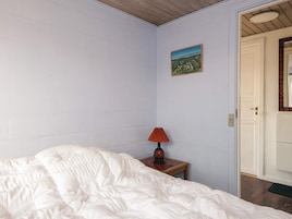 Un dormitorio con cama, mesita de noche con lámpara, una puerta y un cuadro colgado en la pared.