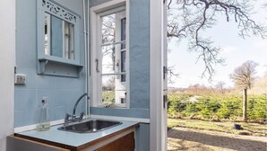 Une cuisine équipée d’un évier, d’une fenêtre et offrant une vue sur un jardin avec des arbres et un chemin en briques.