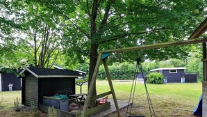 A wooden swing set with a tire swing, a small shed, and a grassy yard with trees. - 4 Person Holiday Home in Hals (Hals)