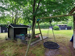 Ein Spielplatz aus Holz mit einer Reifenschaukel, einem kleinen Schuppen und einem grünen Rasen mit Bäumen.