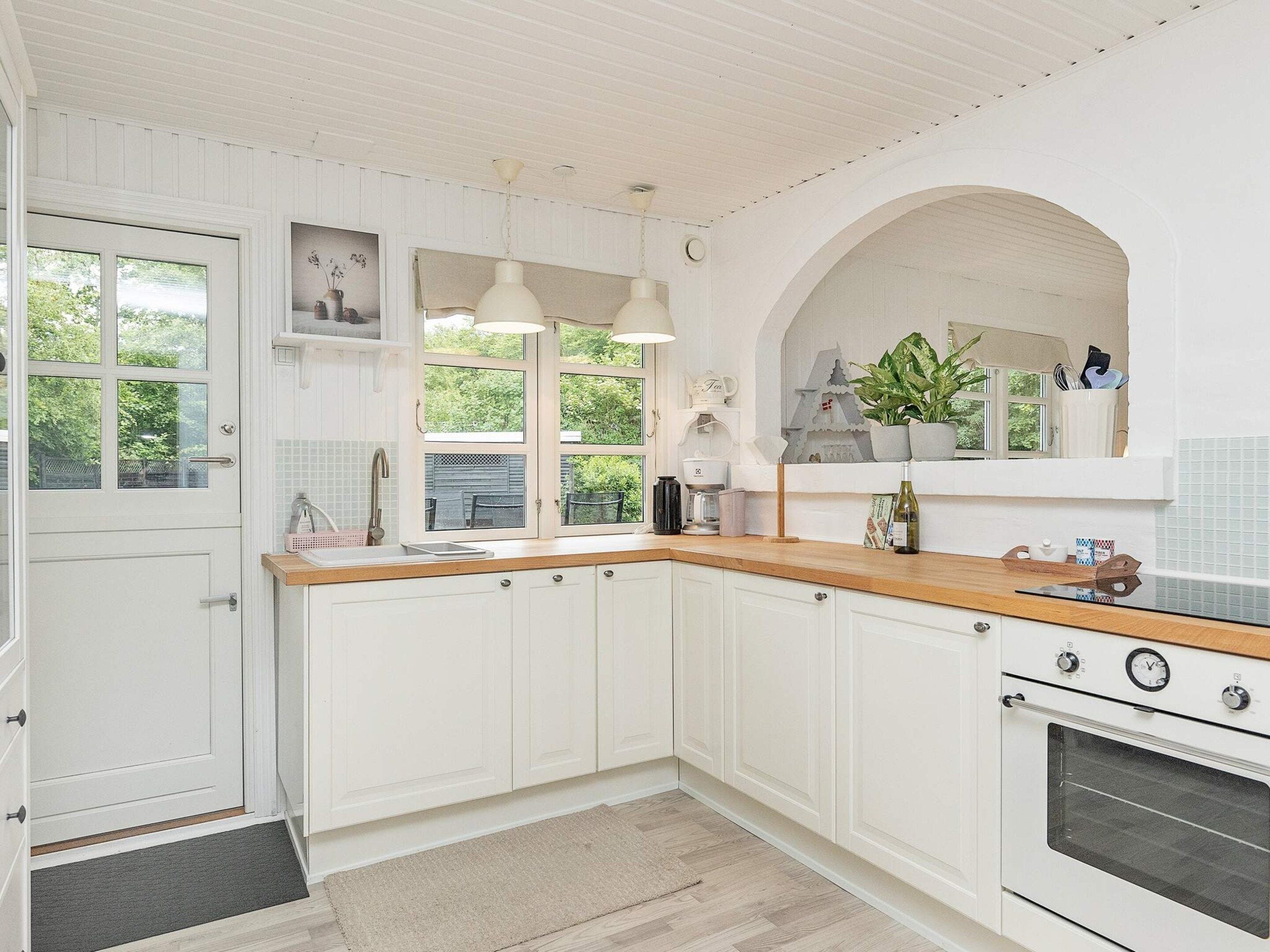 A kitchen with white cabinetry, a wooden countertop, a built-in oven, and a window with a view of greenery outside.