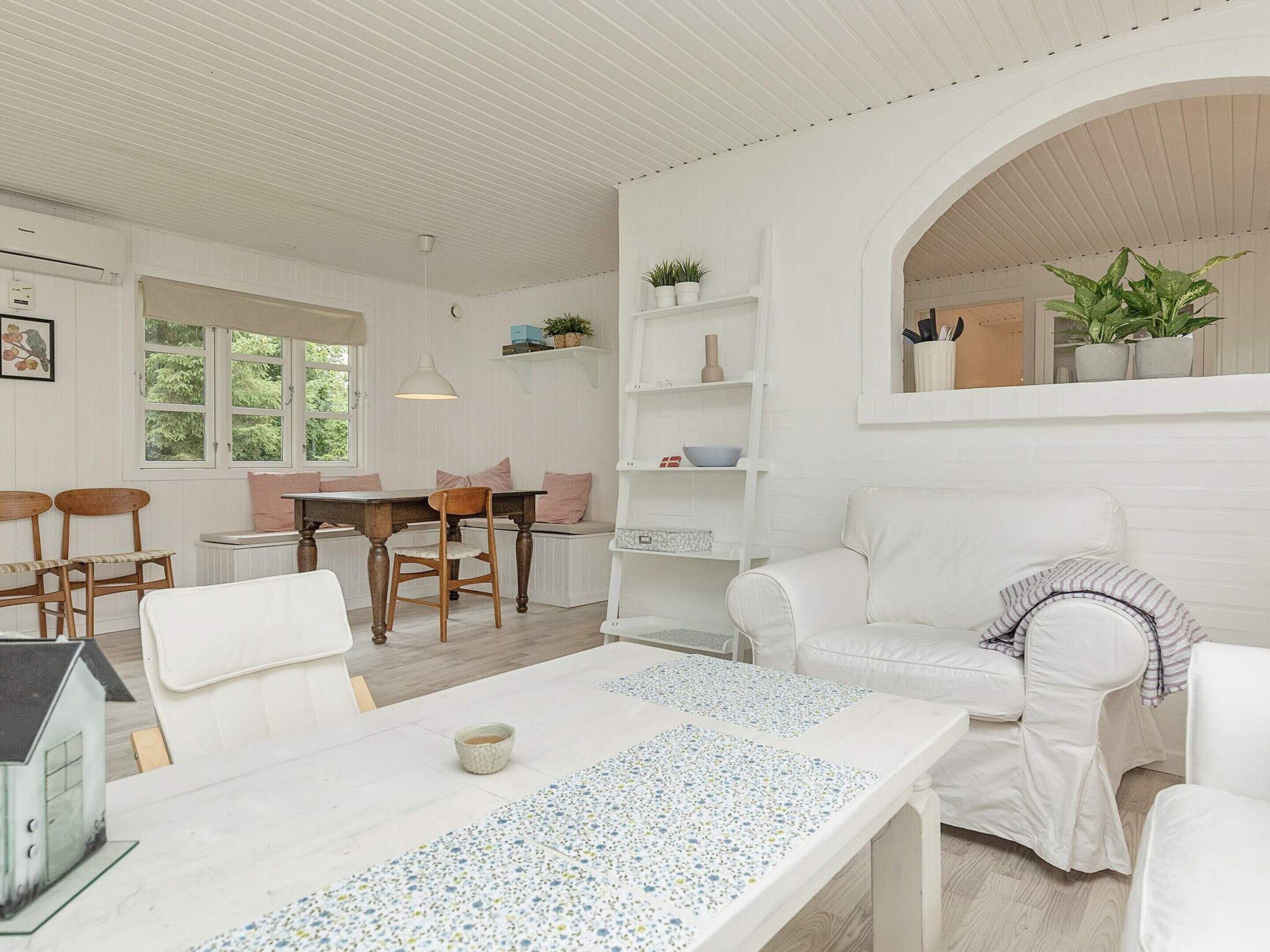 A white-themed living room with a white sofa, a dining table, and a bench.