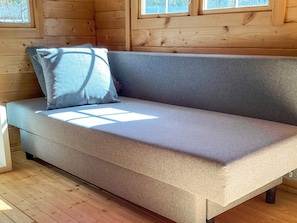 A wooden cabin interior with a gray sofa and a window.