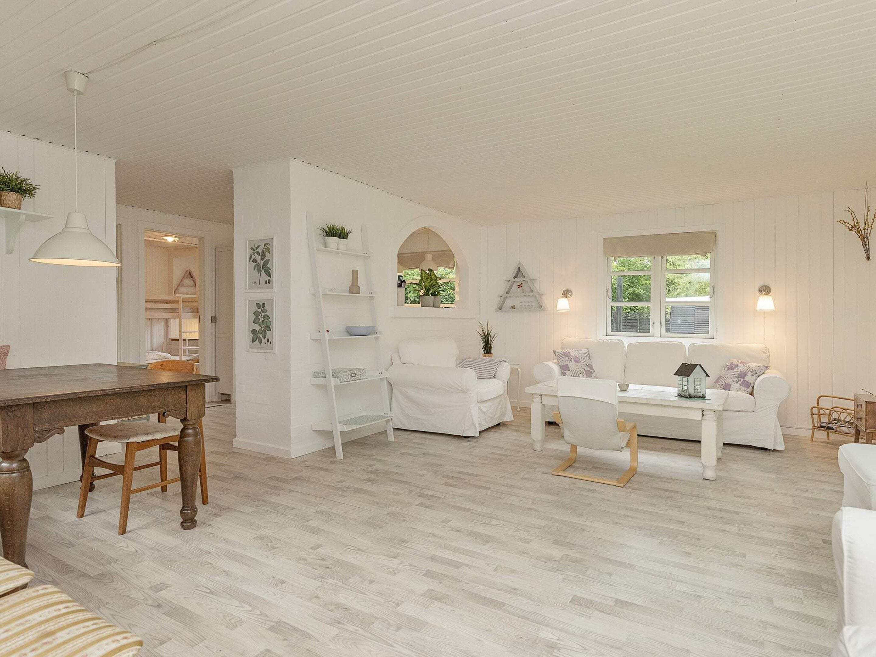 A white-themed living room with a wooden dining table, white sofas, and a white ladder shelf.