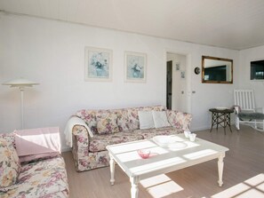 A living room with a floral sofa, a white coffee table, a white armchair, and a floor lamp.
