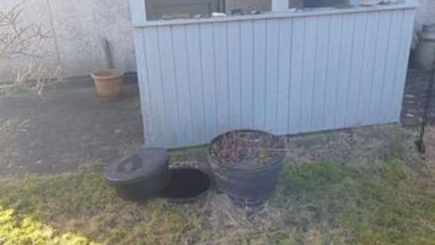 Edificio con ventana, puerta y un pequeño espacio exterior con un contenedor de basura y un neumático.