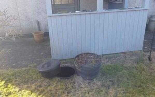 A building with a window, a door, and a small outdoor area with a trash bin and a tire.