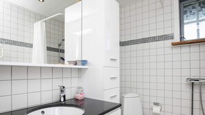 Un baño moderno con un lavamanos blanco, encimera negra y un inodoro. Hay un espejo sobre el lavamanos y una ventana sobre el inodoro.