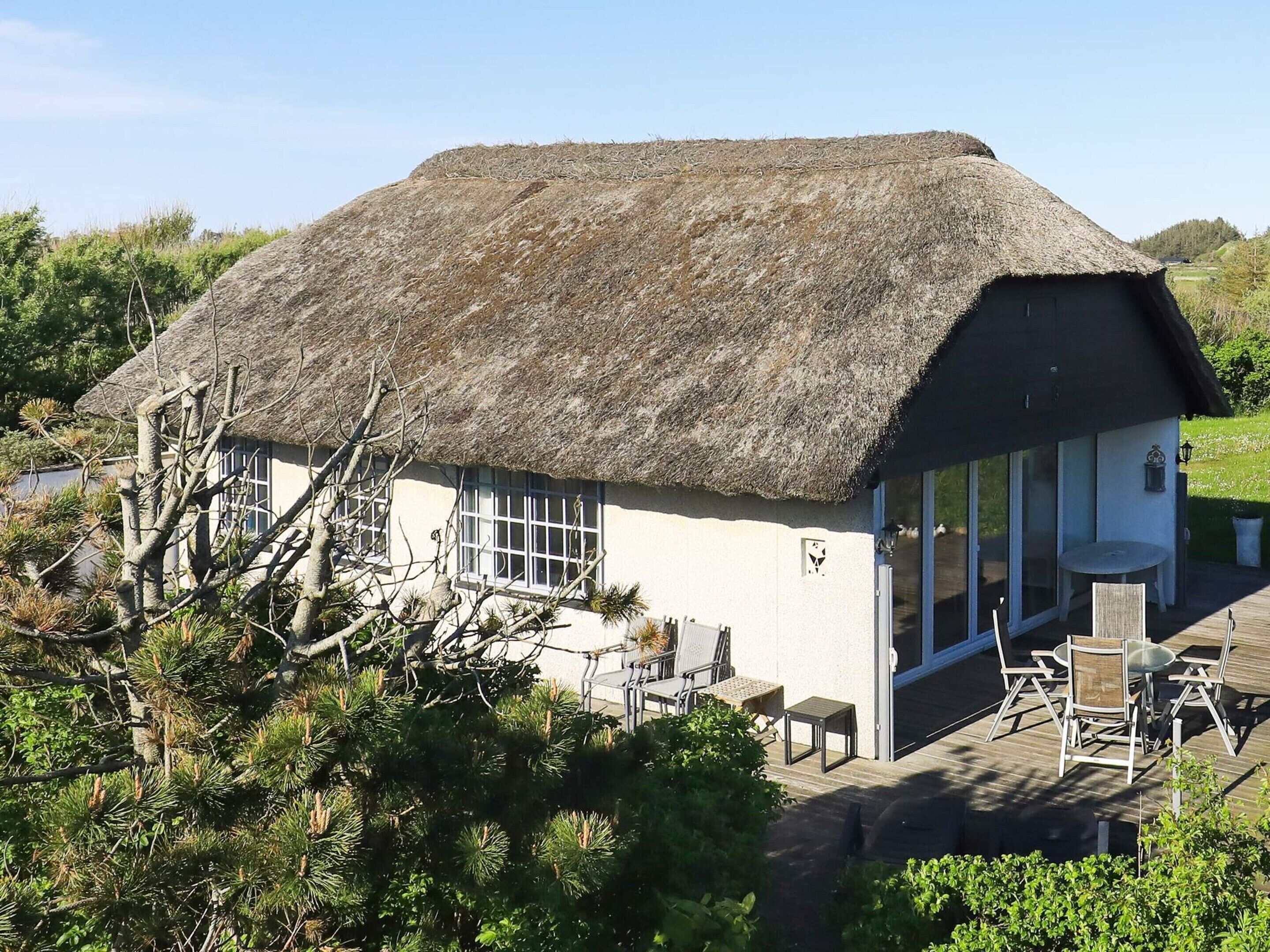 A thatched-roof house with a patio area, surrounded by greenery.