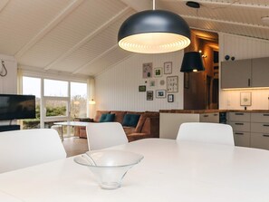 Una cocina moderna con armarios blancos, un comedor con mesa y sillas blancas, y una lámpara colgante negra grande.
