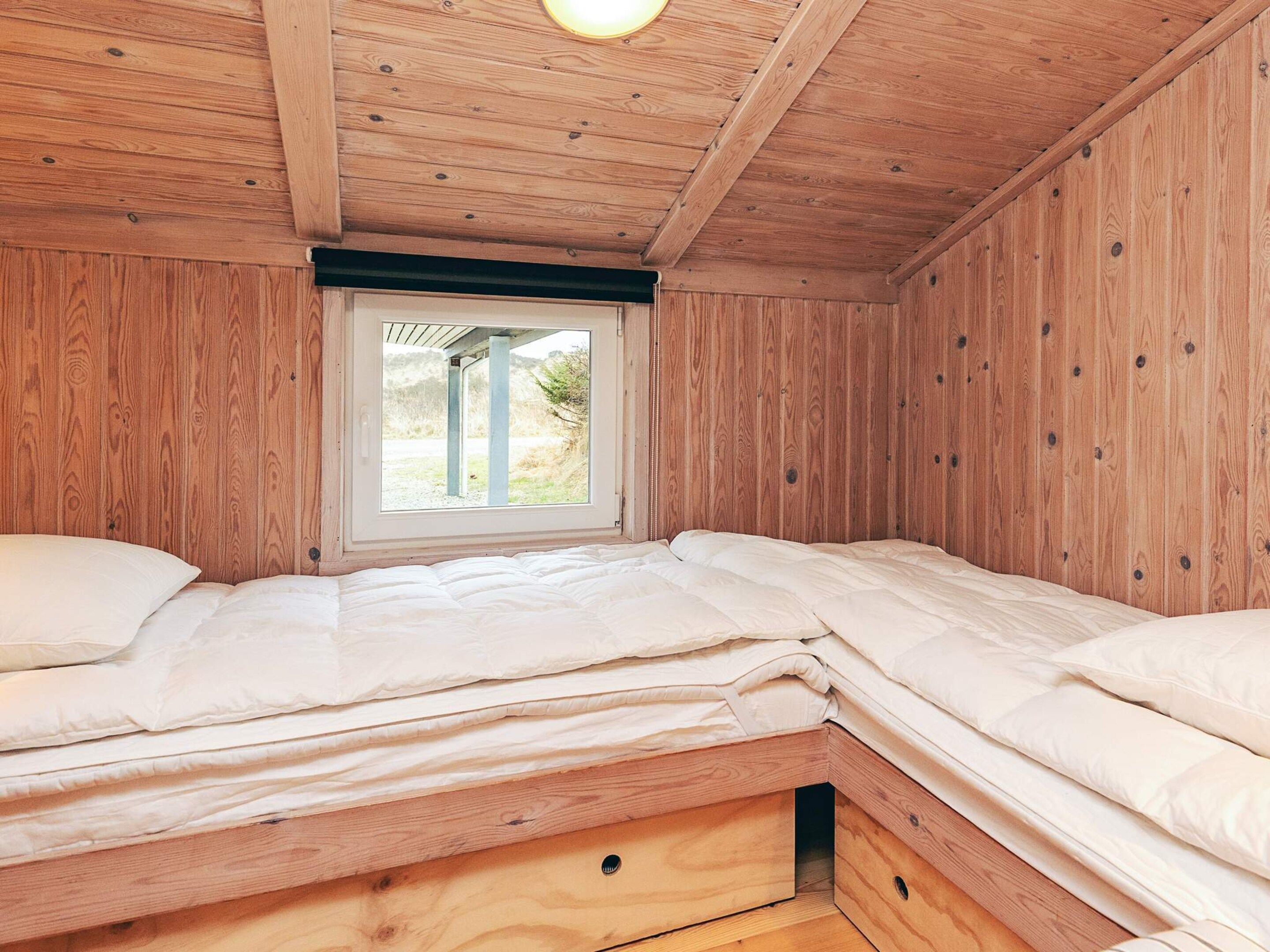 A small, wooden-paneled room with a single bed and a window providing a view of the outdoors.