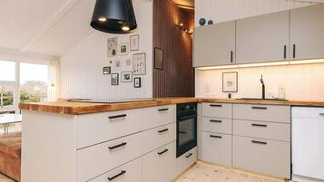 Una cocina moderna con armarios blancos, encimera de madera y lámpara colgante negra.